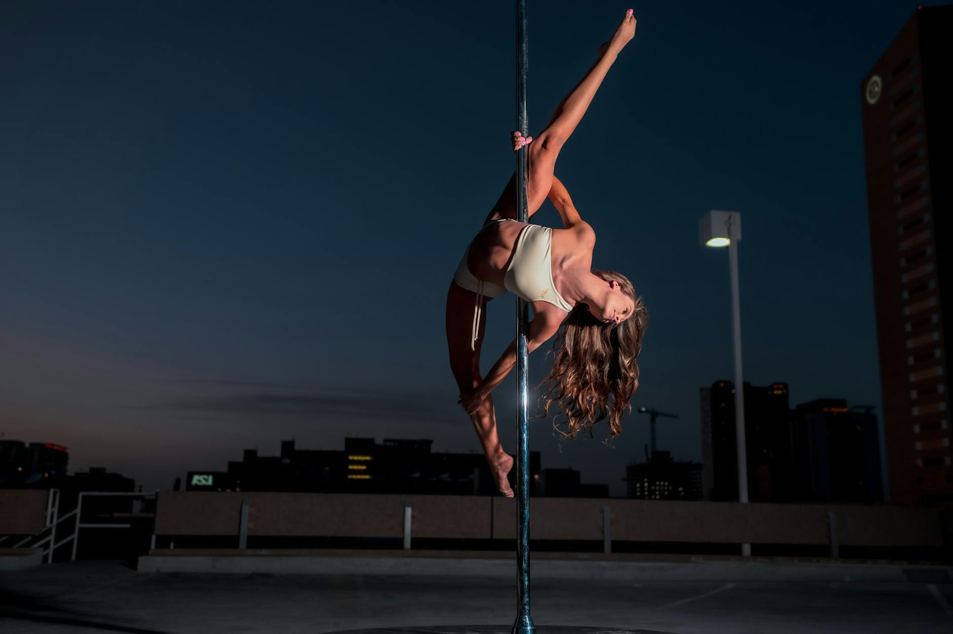 Tancerka pole dance wykonuje figurę na dachu z nocną panoramą miasta
