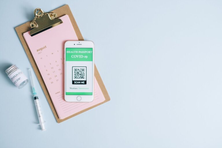 Smartfon z paszportem covidowym obok strzykawki i fiolki szczepionki